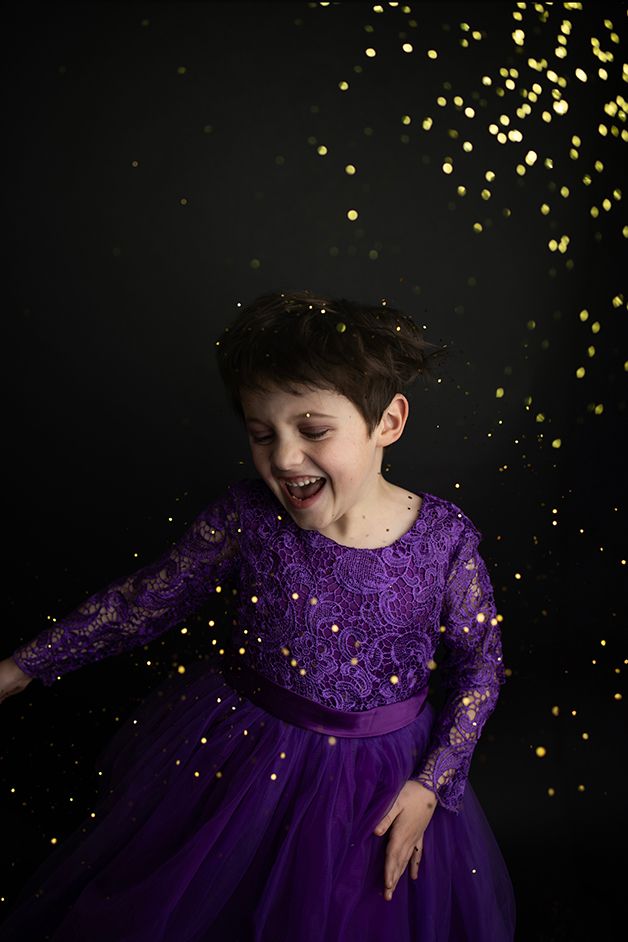 Little boy in purple dress dancing and smiling with gold glitter all around.