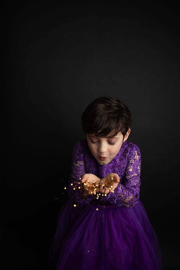 Little boy in purple dress blowing gold glitter.