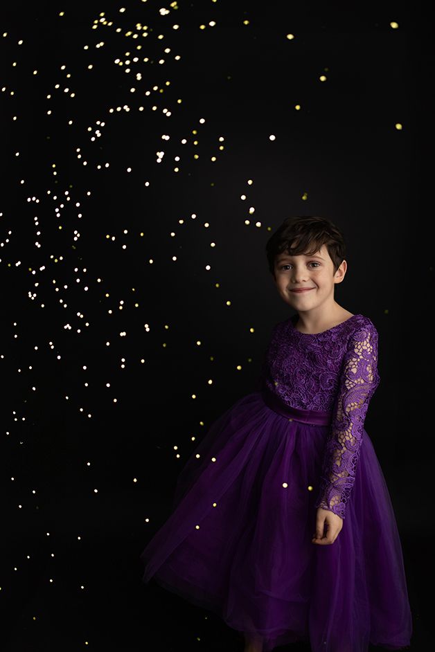 Little boy in purple dress dancing with gold glitter falling all around.