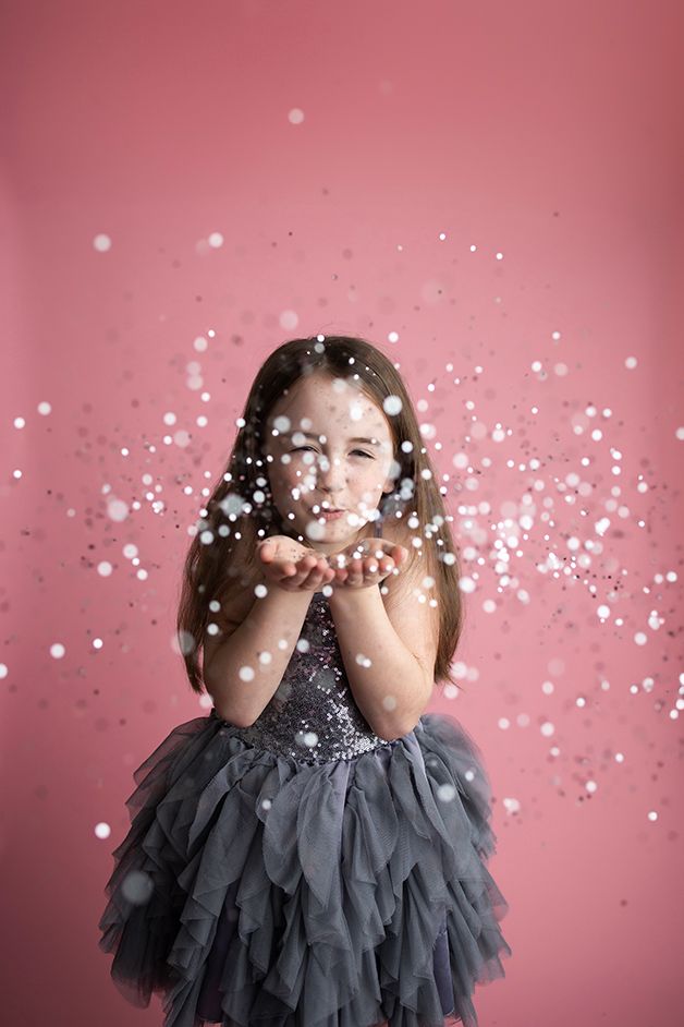 Little girl in grey dress blowing silver glitter.