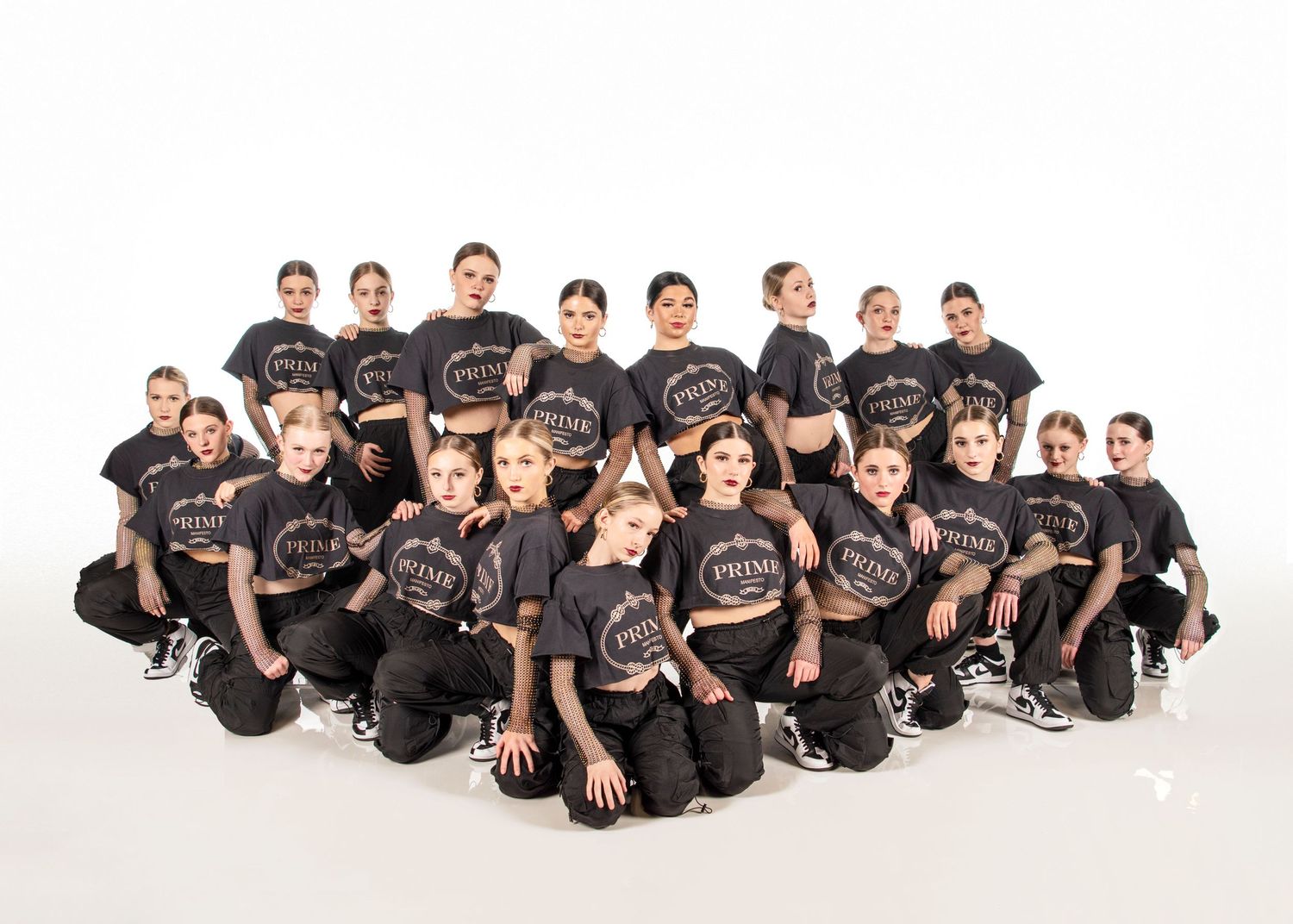 A dance team wearing matching black t-shirts and pants poses together in a group studio photo.
