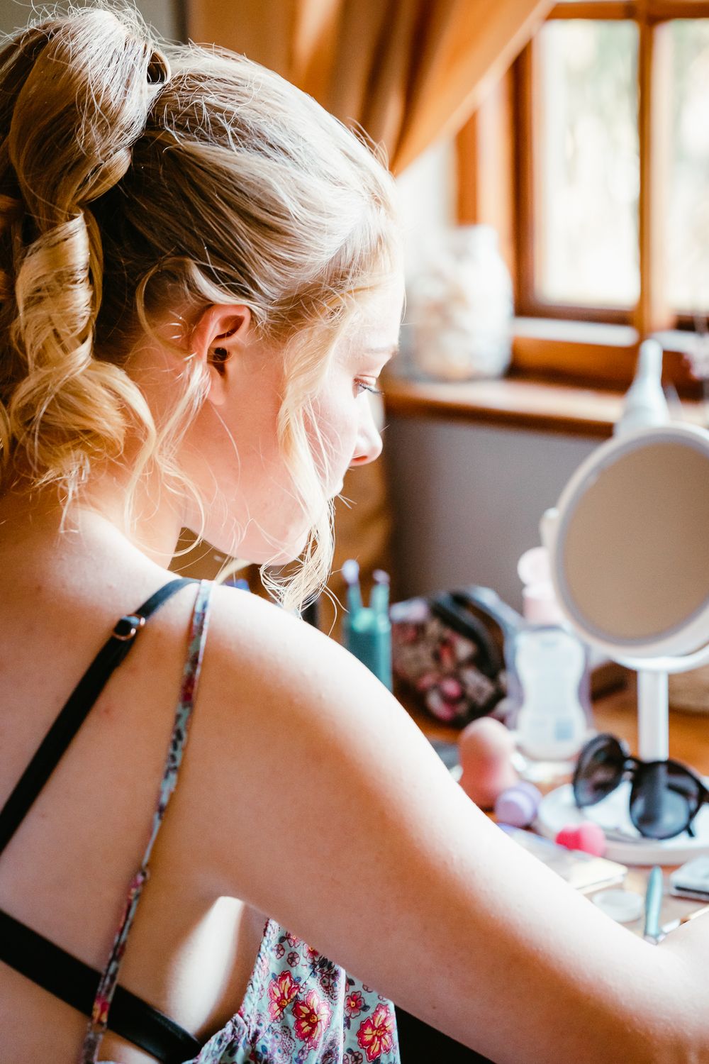 Young woman with blonde updo hair applying makeup in front of small mirror