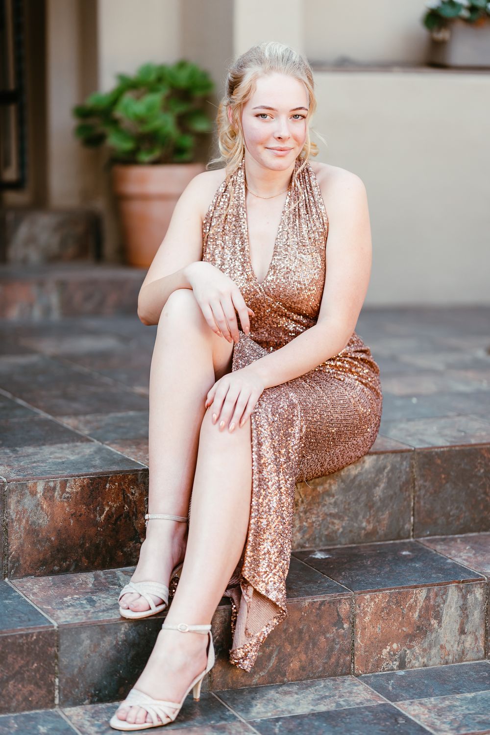 Young blonde-haired woman in a rose gold dress sitting on stone steps