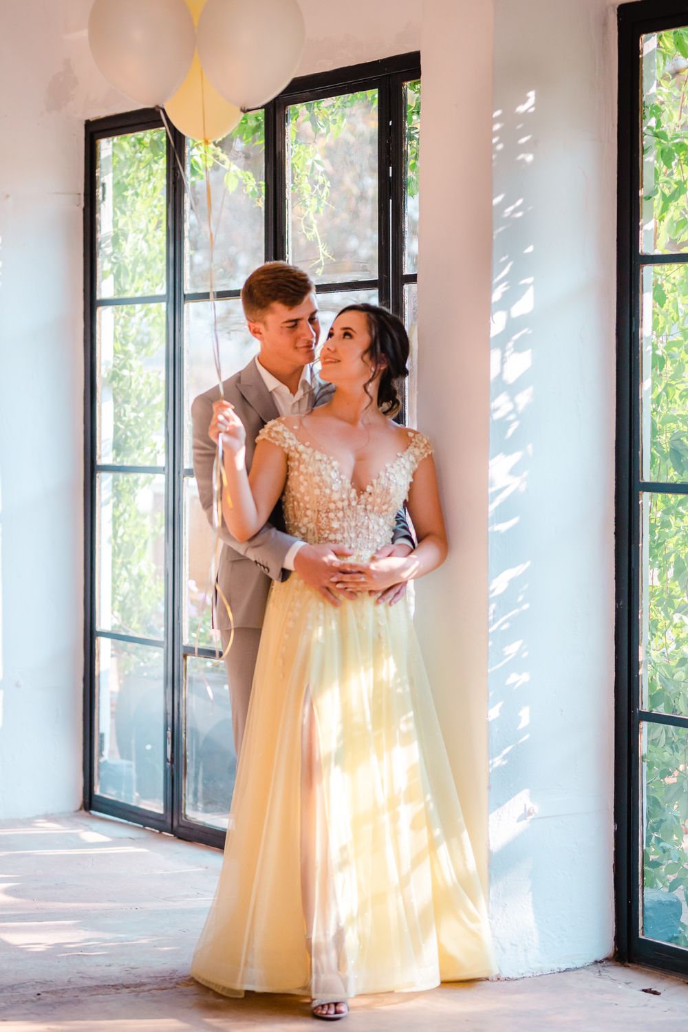 Young senior couple embracing in front of large windows with soft sunlight streaming through