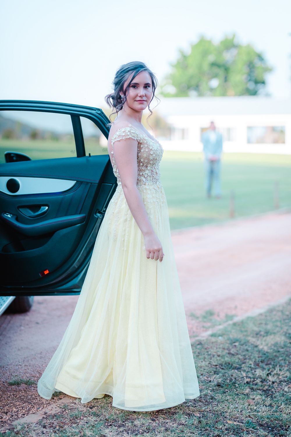 Young dark haired woman standing next to a dark car with the door open and young male in the background