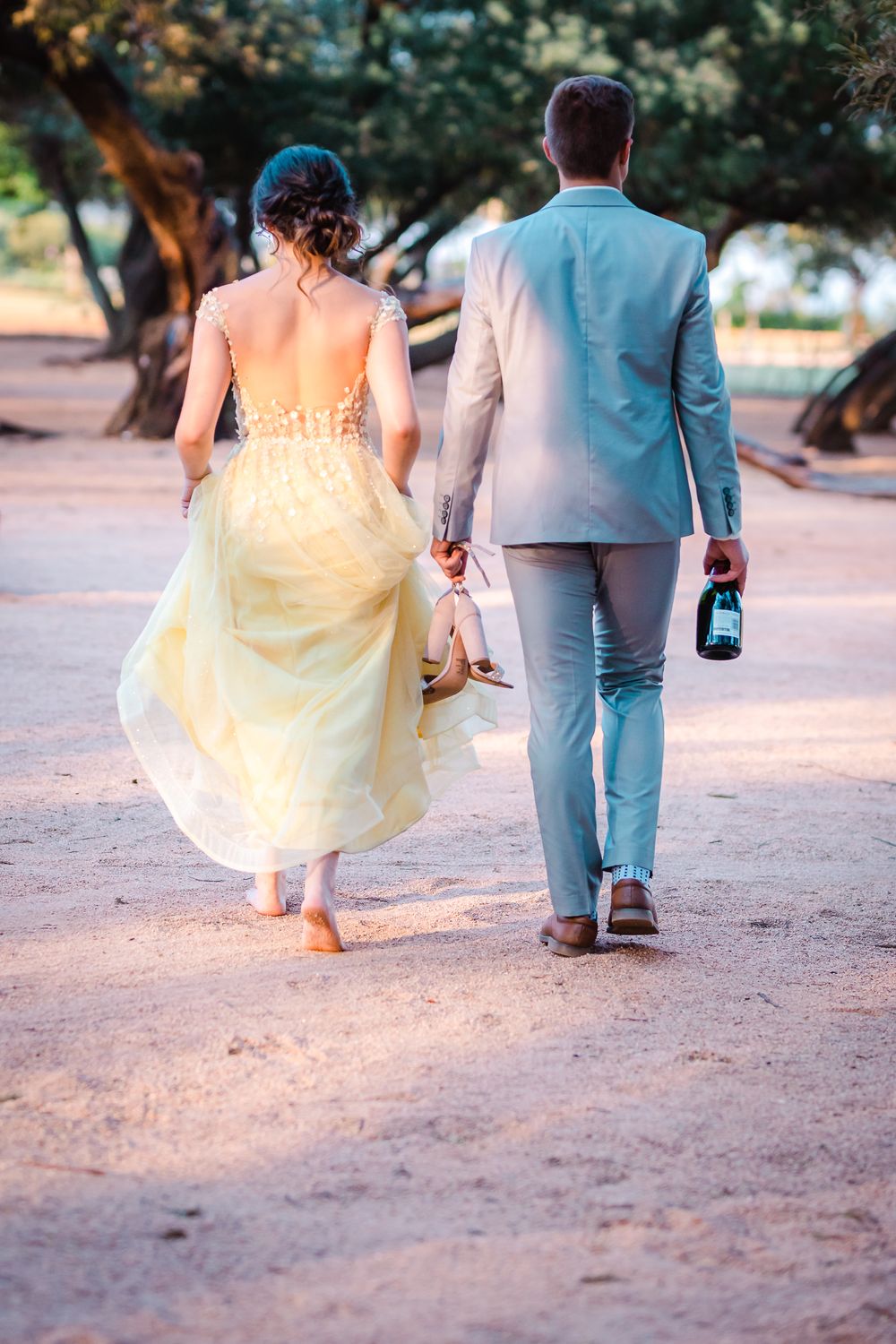 Young couple walking away from the camera male is holding girls shoes and a bottle of bubbly