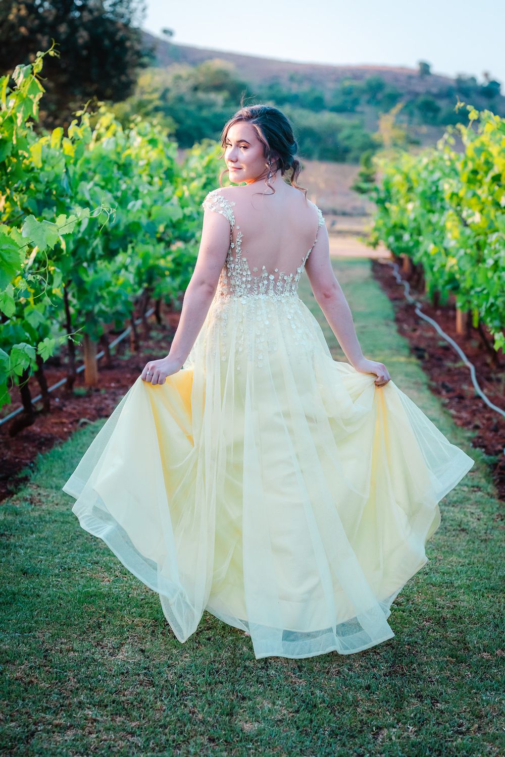 Young dark-haired woman in yellow dress walking in the vineyard looking over her shoulder