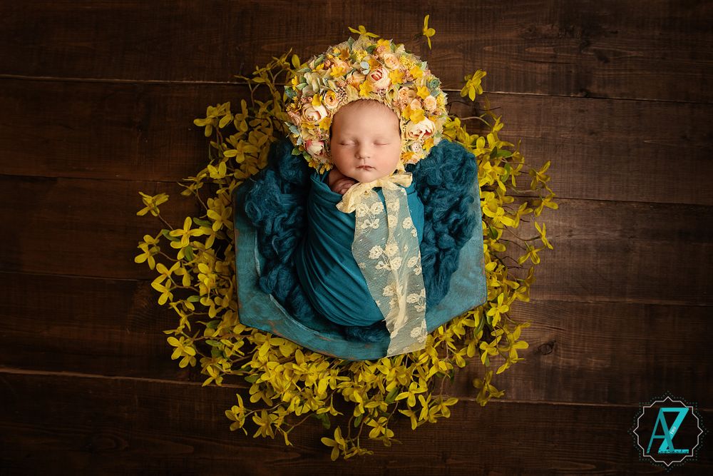 Wrapped newborn surrounded by yellow forsythia flowers in circular arrangement.