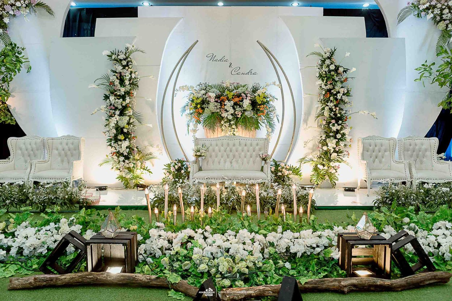 Luxurious white and green wedding stage with floral arrangements and modern curved backdrop.