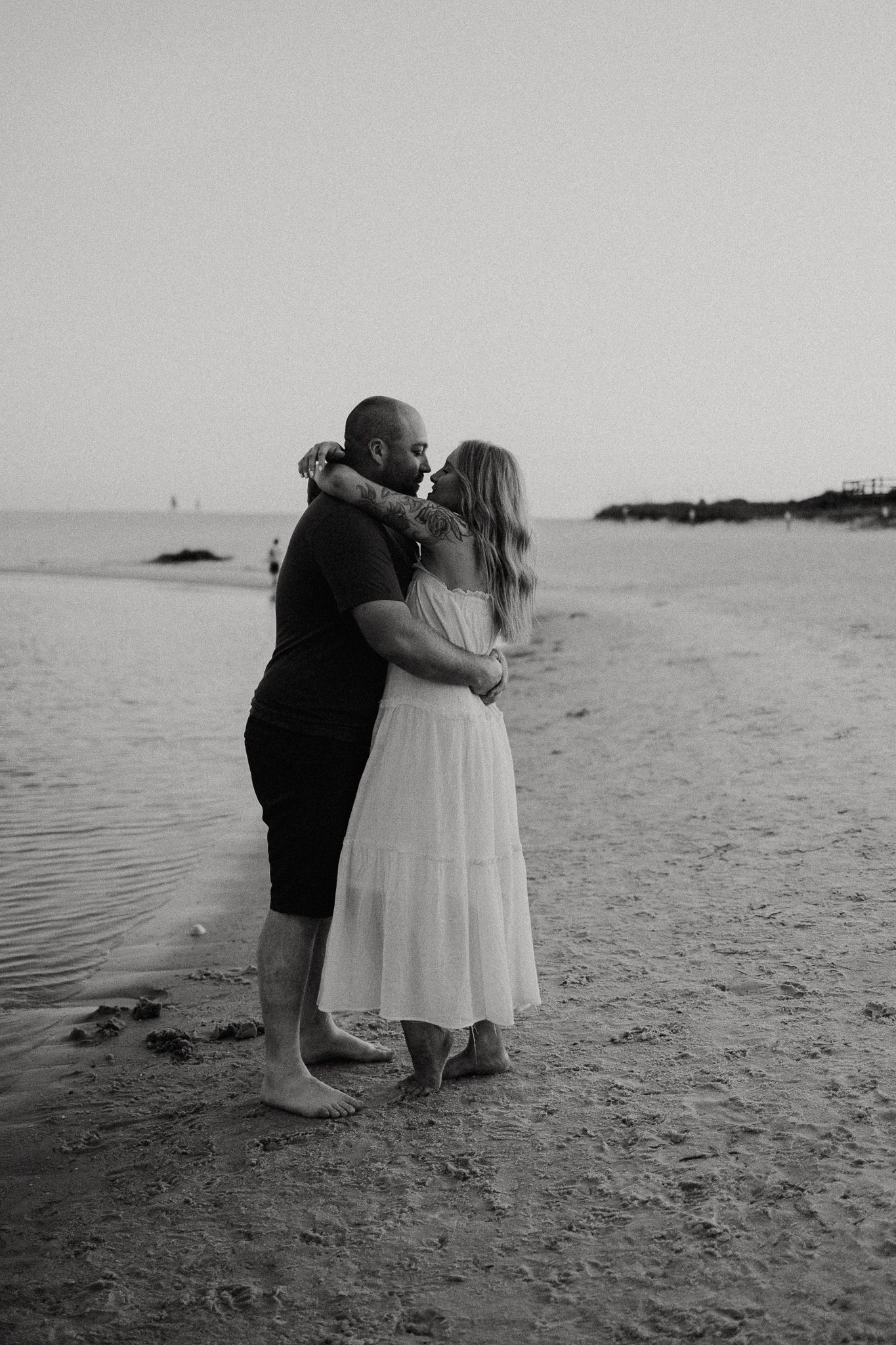A romantic black and white photo of a couple embracing on a beach at sunset.