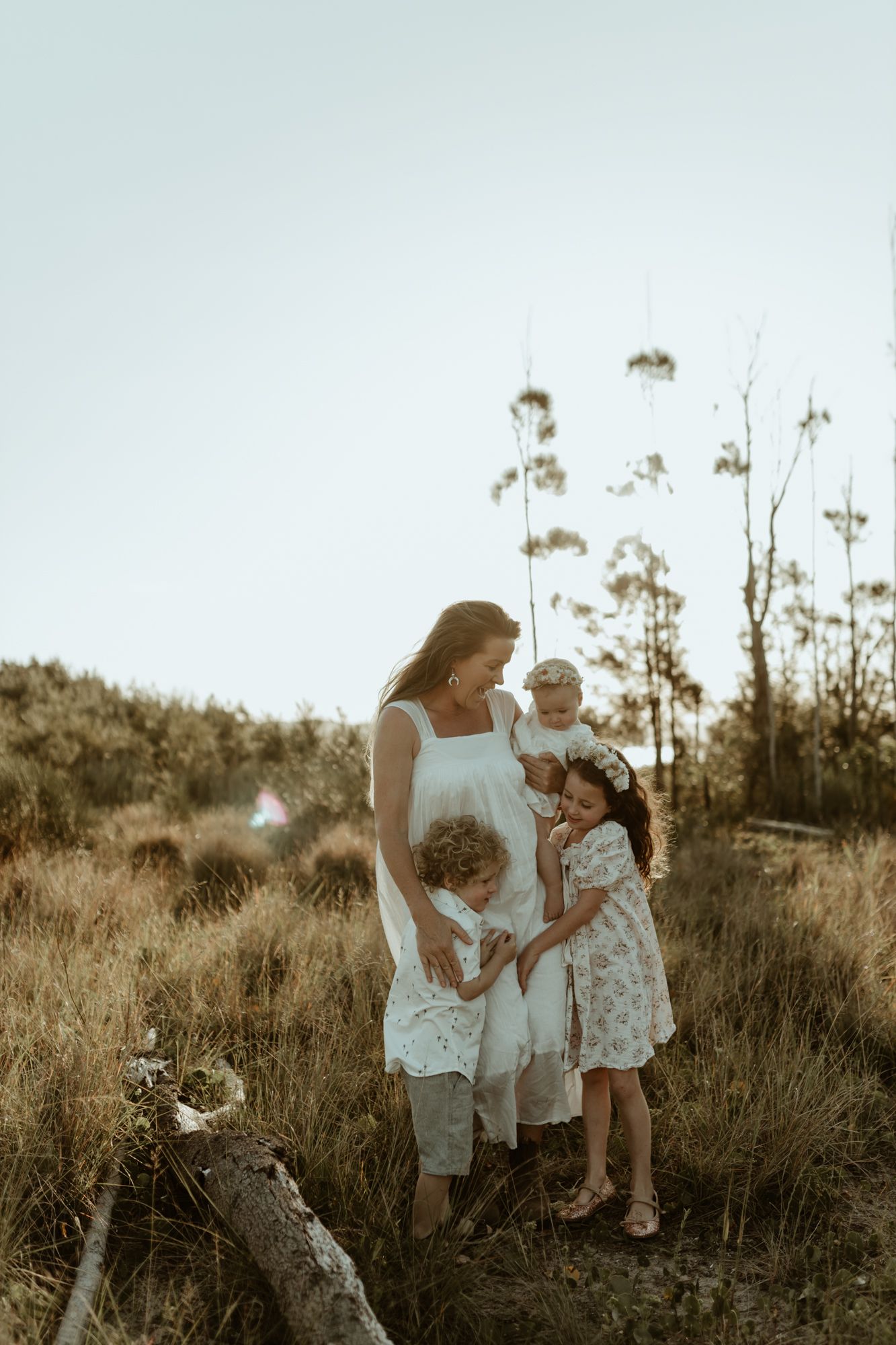 A warm family portrait amidst tall grass and trees during sunset.