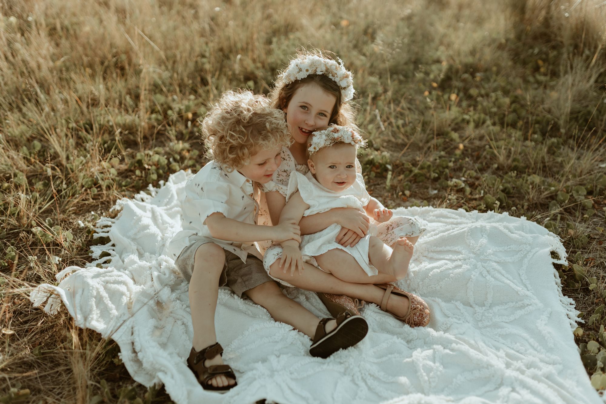 A tender family moment on a white blanket in a golden field during sunset.