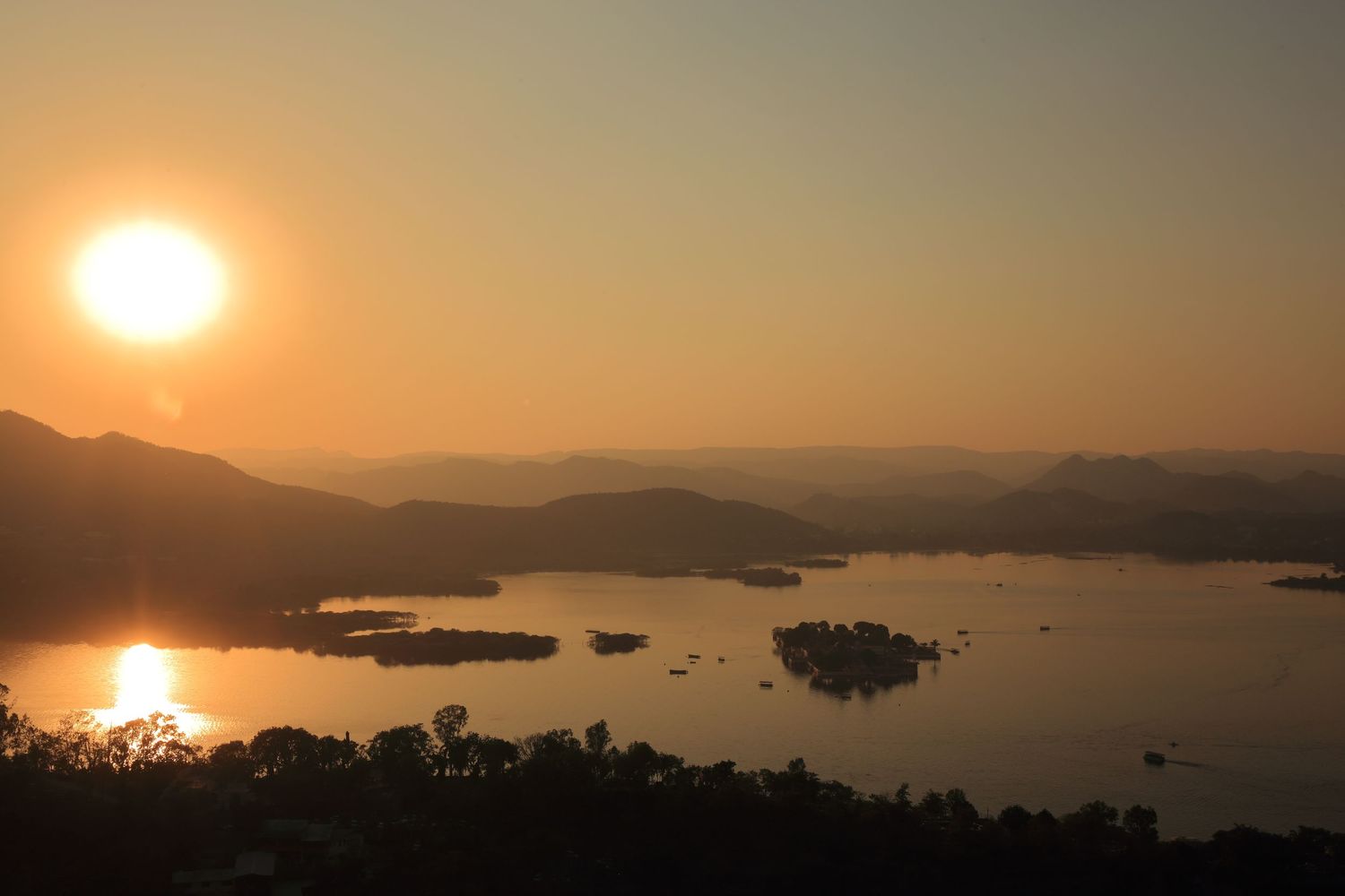 Sunset over Lake Pichola with silhouetted mountains and islands in Udaipur.