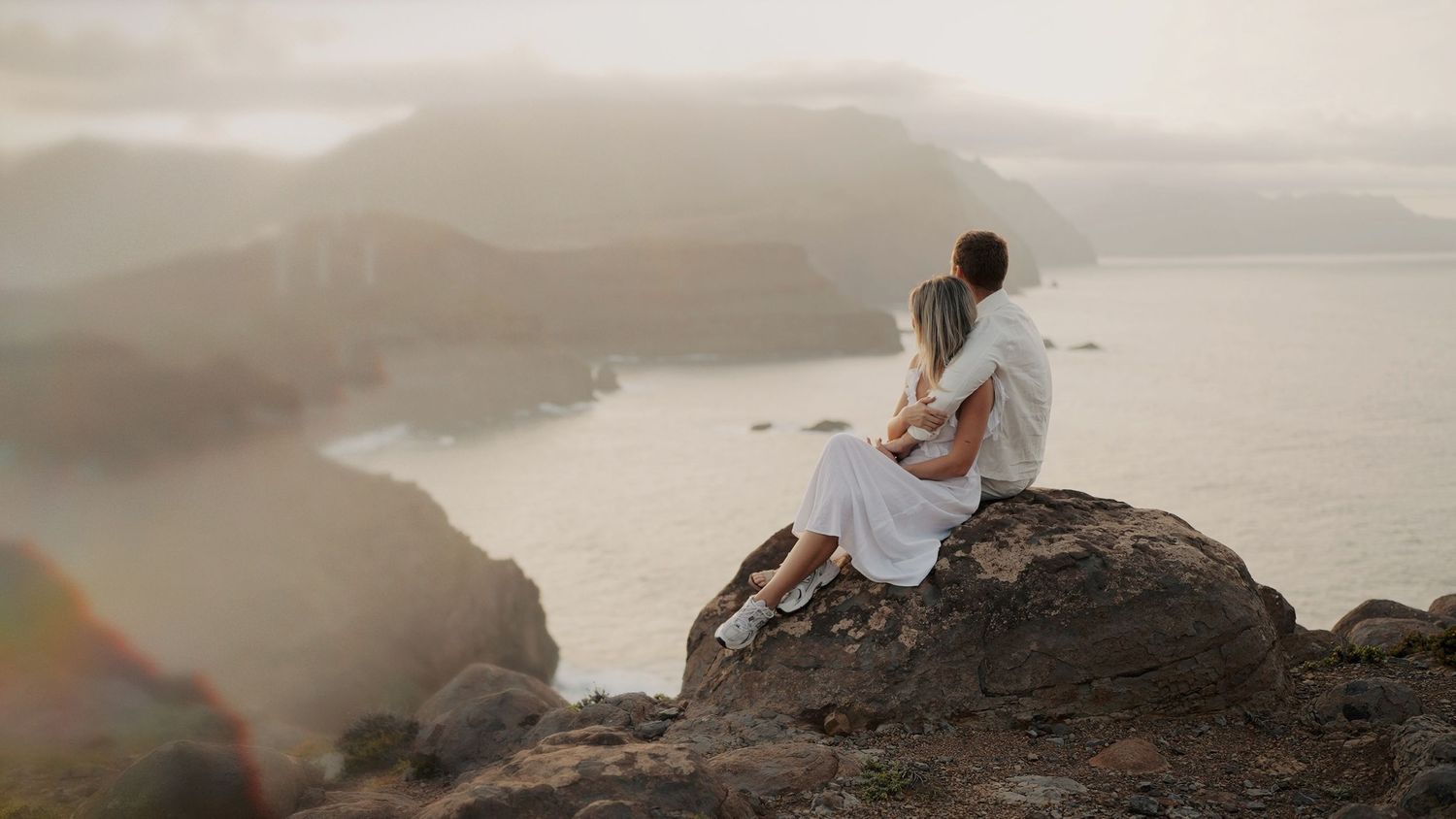 Couple exploring rocky coastal formations during sunset.