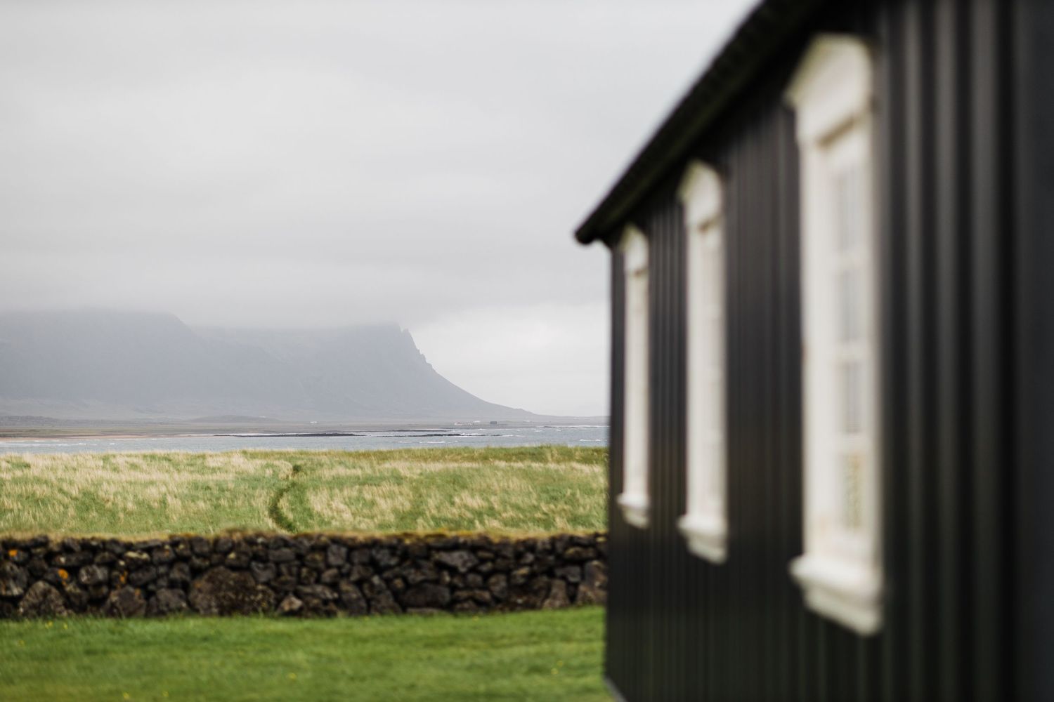 Dark wooden building with white windows overlooking a misty coastal landscape and green fields.