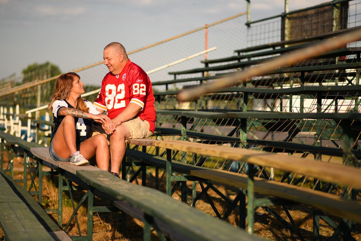 A couple sits together on bleachers at sunset wearing casual attire.