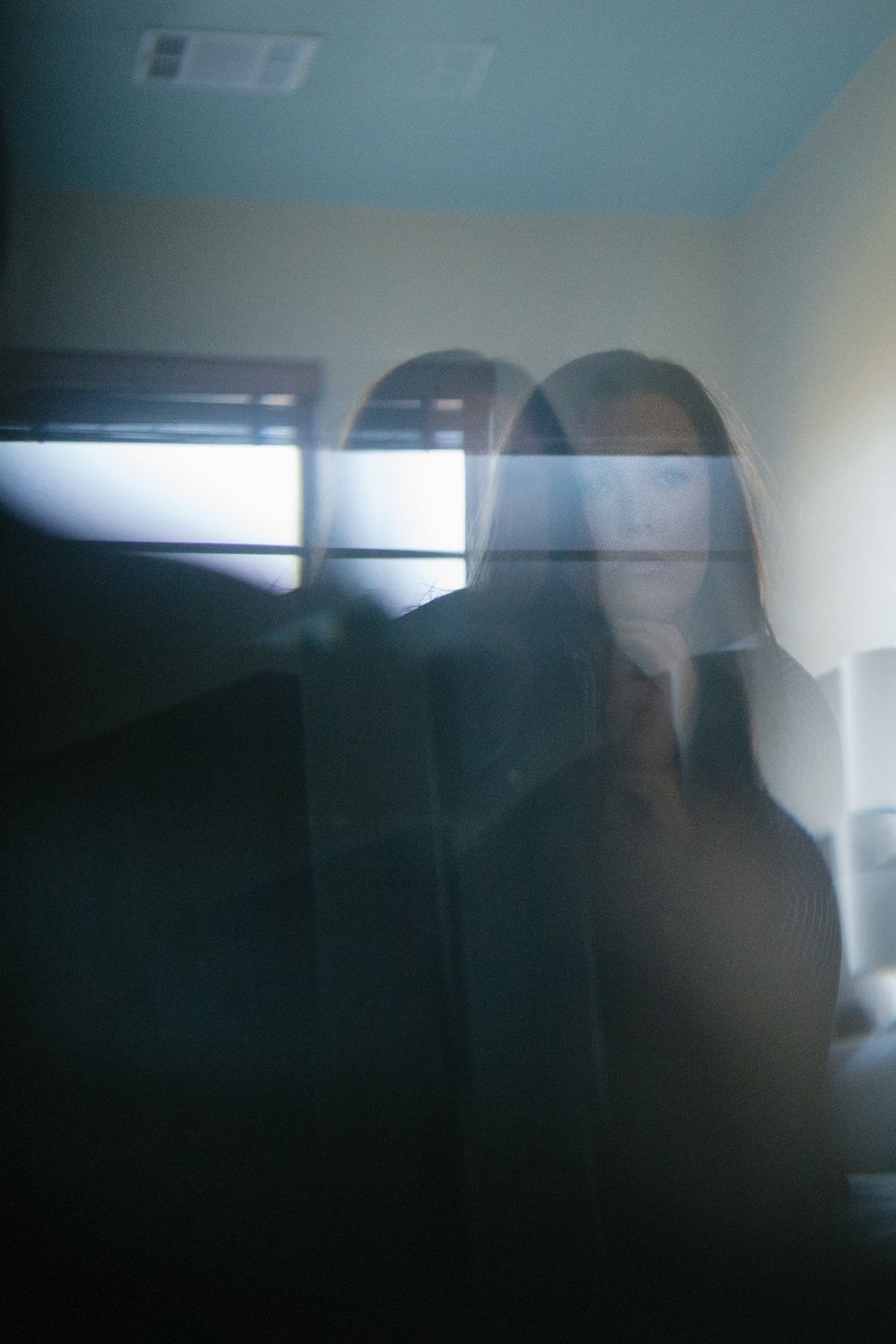 double reflection of woman in a beveled mirror, back lit by a bright window