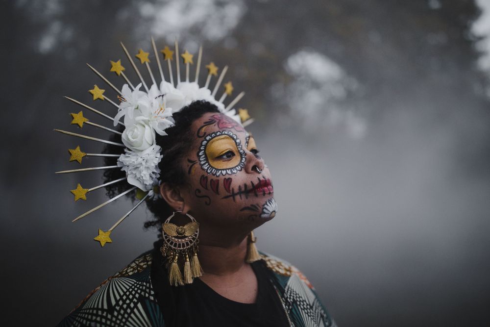 Latinx Black femme wearing traditional Dia de los Muertos facepaint, flower crown, and clothing in fog, Boston TX