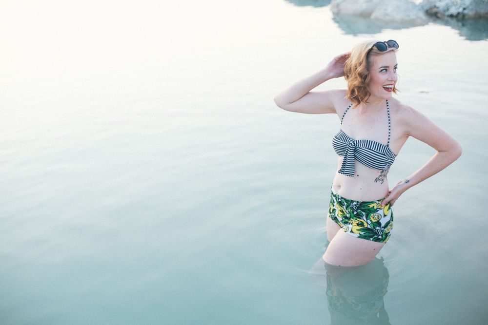 woman laughing, pinup pose, vintage swimwear, thigh deep in aqua blue water in abandoned limestone quarry, Texas