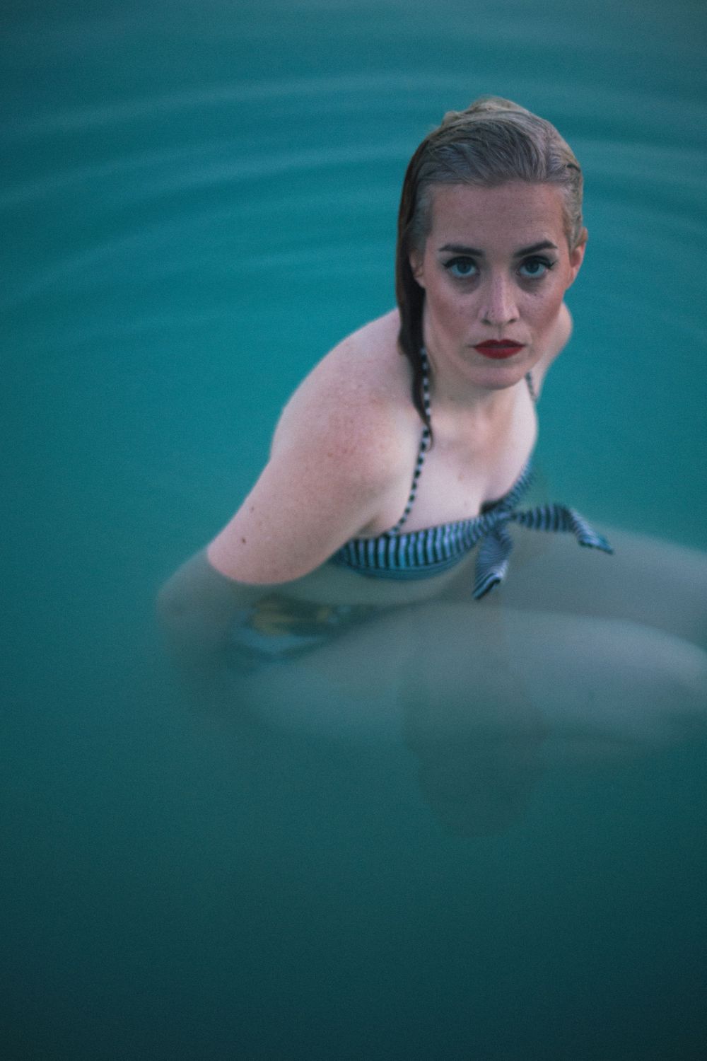 blond woman with red lipstick, wearing vintage swimwear swimming in aqua blue water, in abandoned limestone quarry, TX