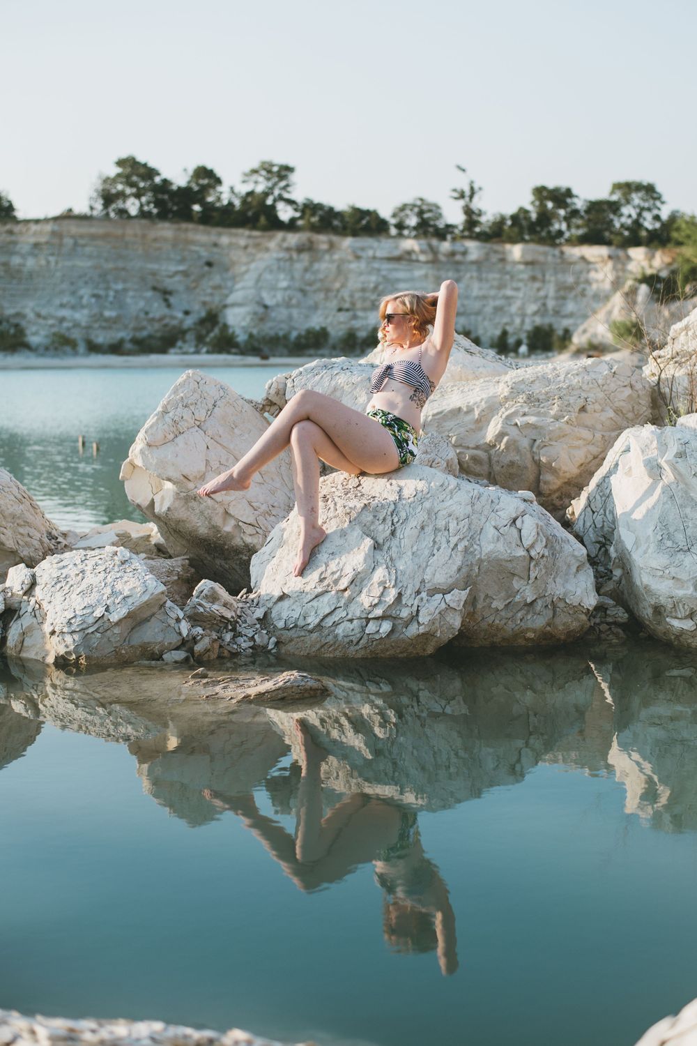 woman sitting on white rocks in abandon limestone quarry, mckinney TX, aqua blue water reflecting pinup swimwear pose