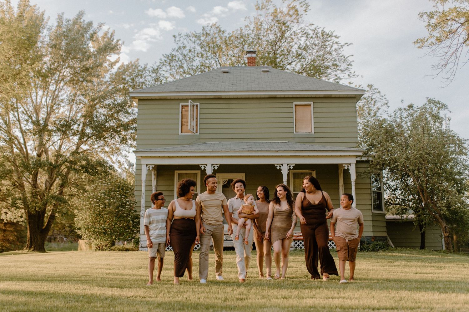 Group photo of people standing together in front of a classic farmhouse on a sunny day.