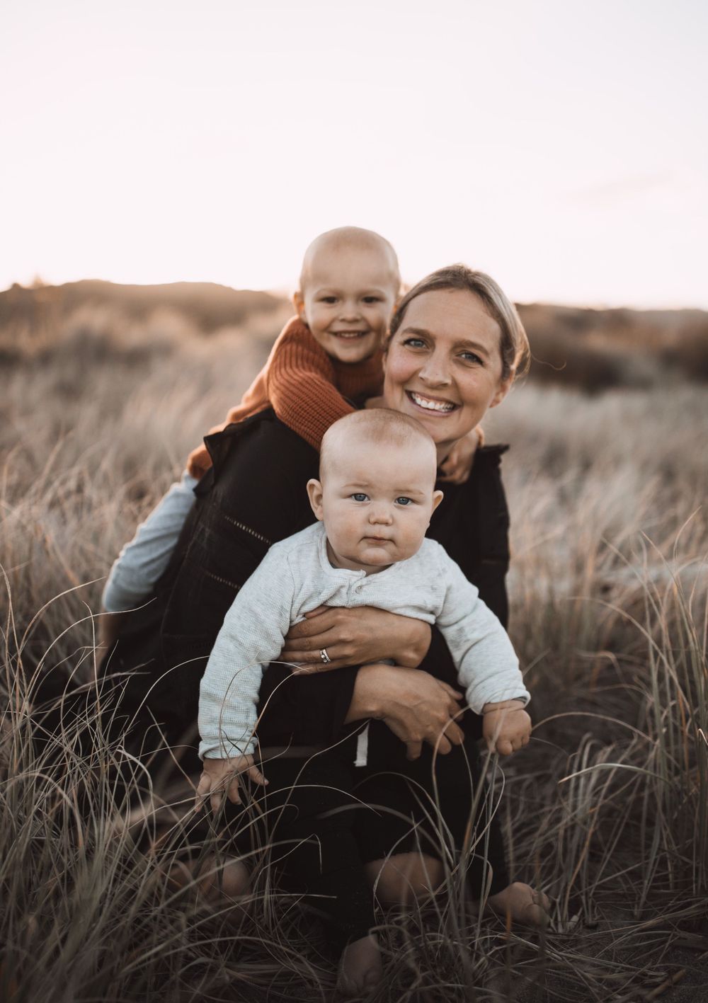 Family enjoying playful moments together in field of dried grass at dusk.