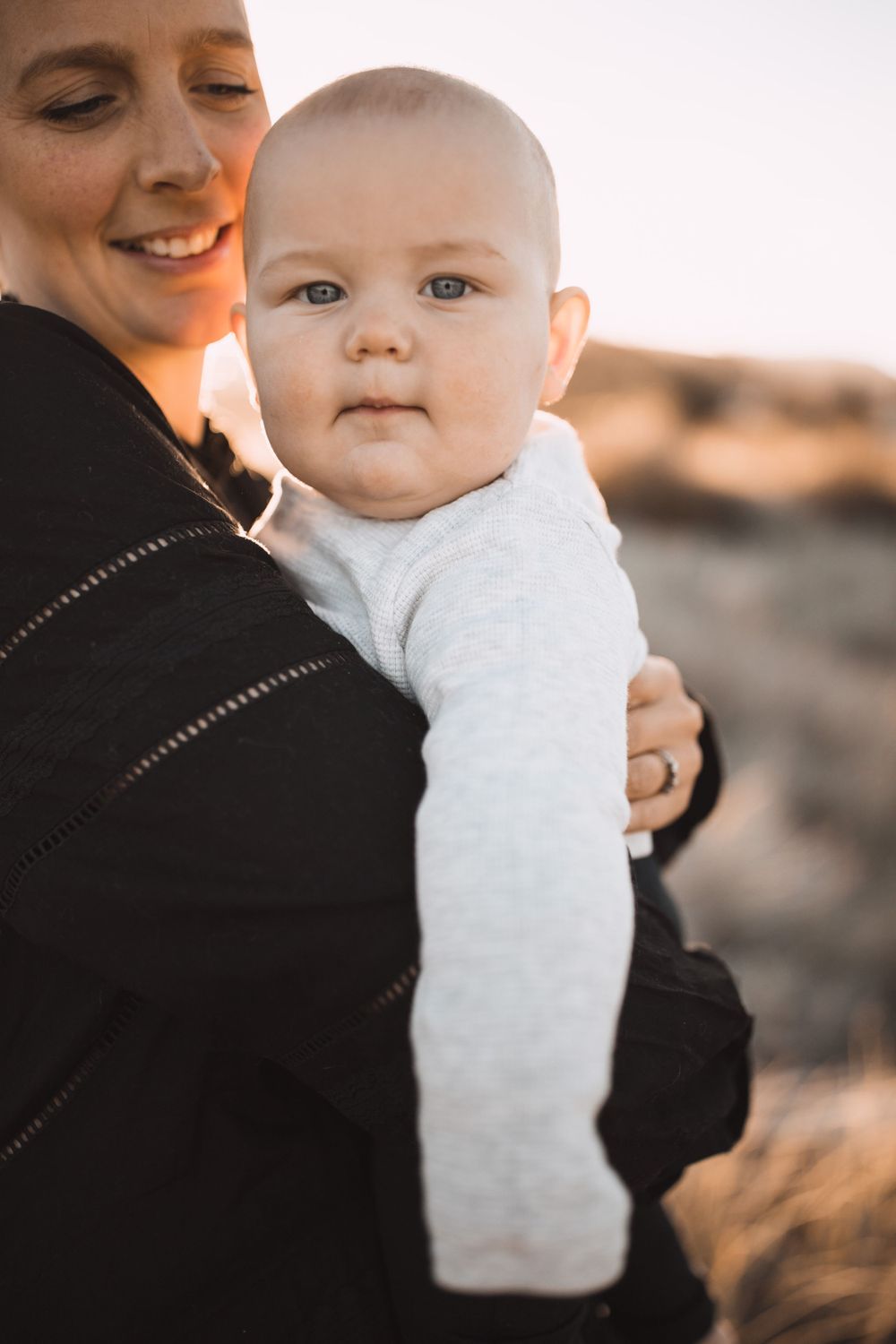 Parent and baby share tender moments against golden sunset in outdoor portrait series.