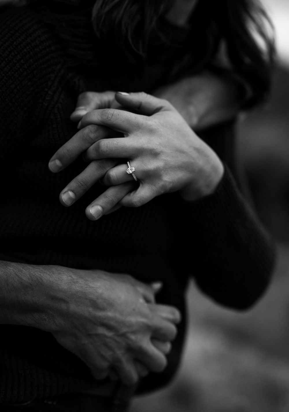 Black and white close-up of hands with engagement ring in intimate embrace.