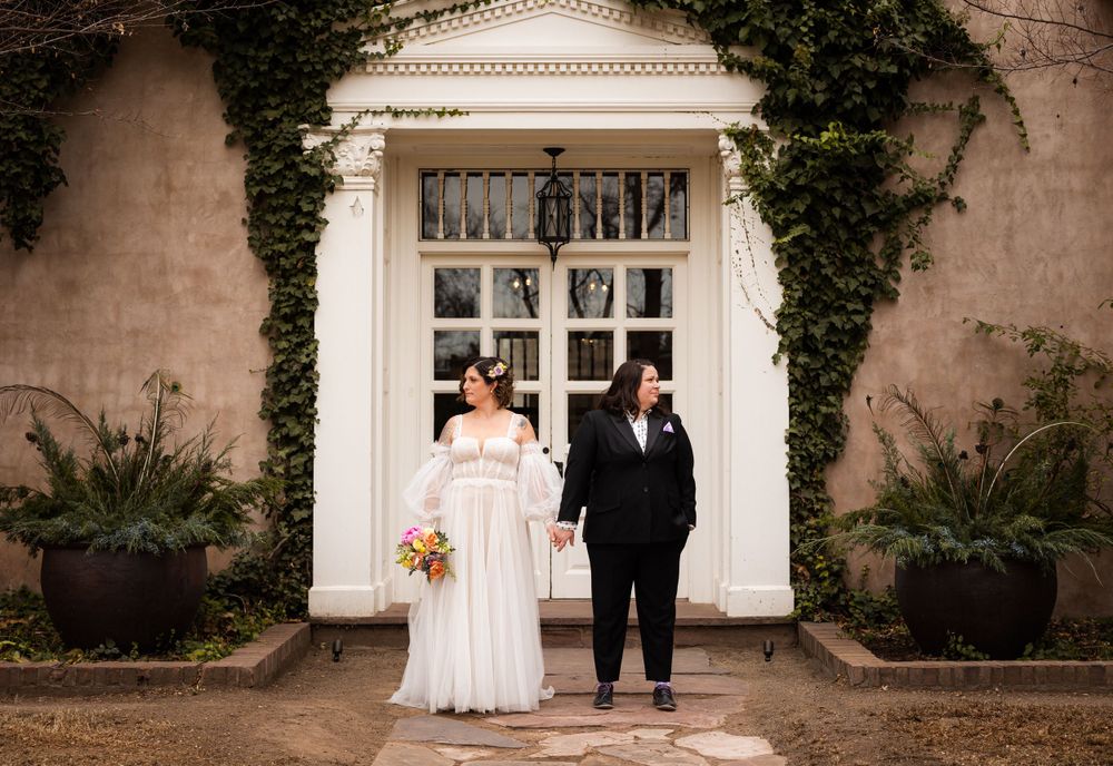 A couple stands in front of an elegant white doorway framed by climbing ivy and ferns during their wedding.