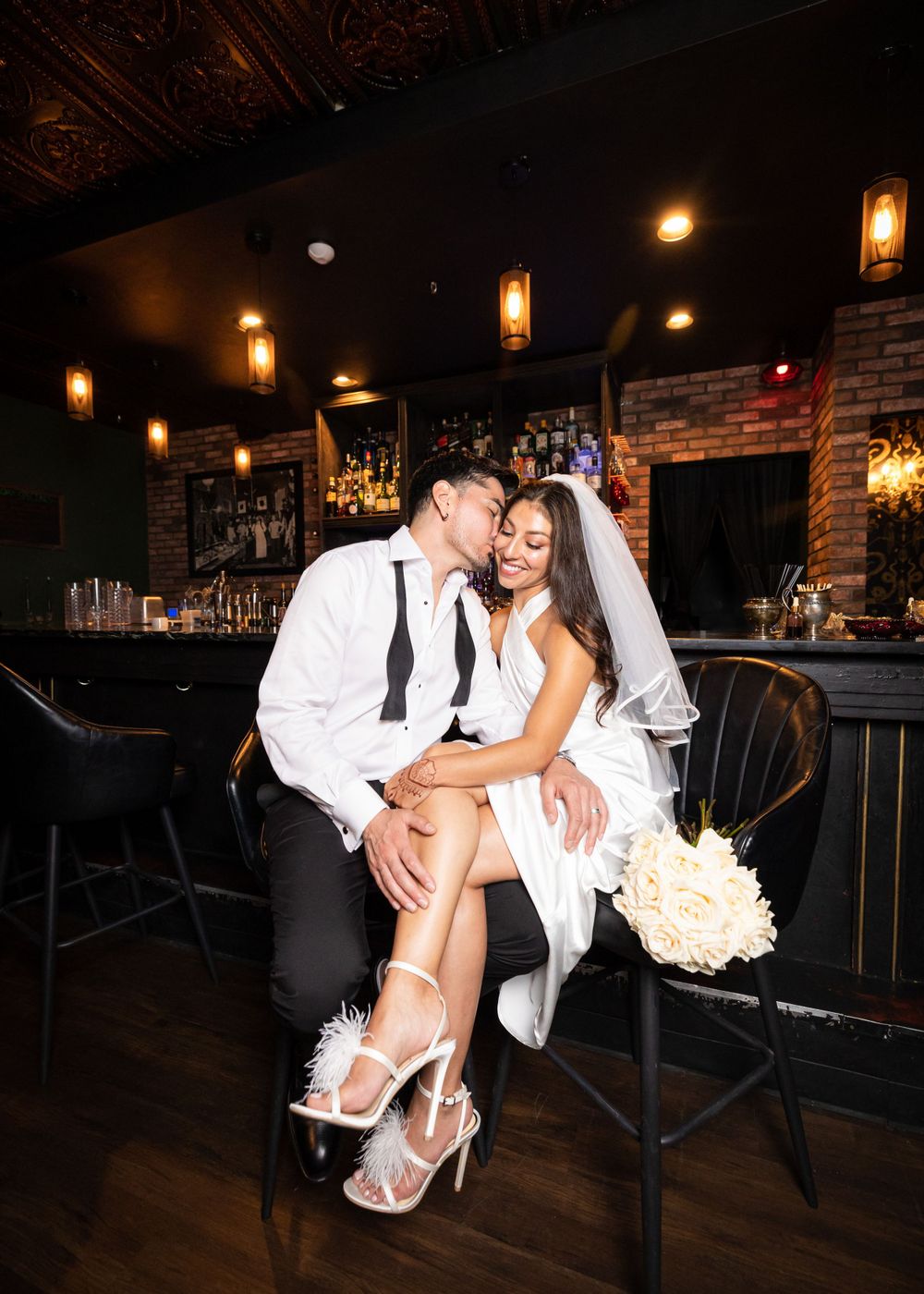 Newlyweds share an intimate moment at a dimly lit bar with vintage lighting fixtures.