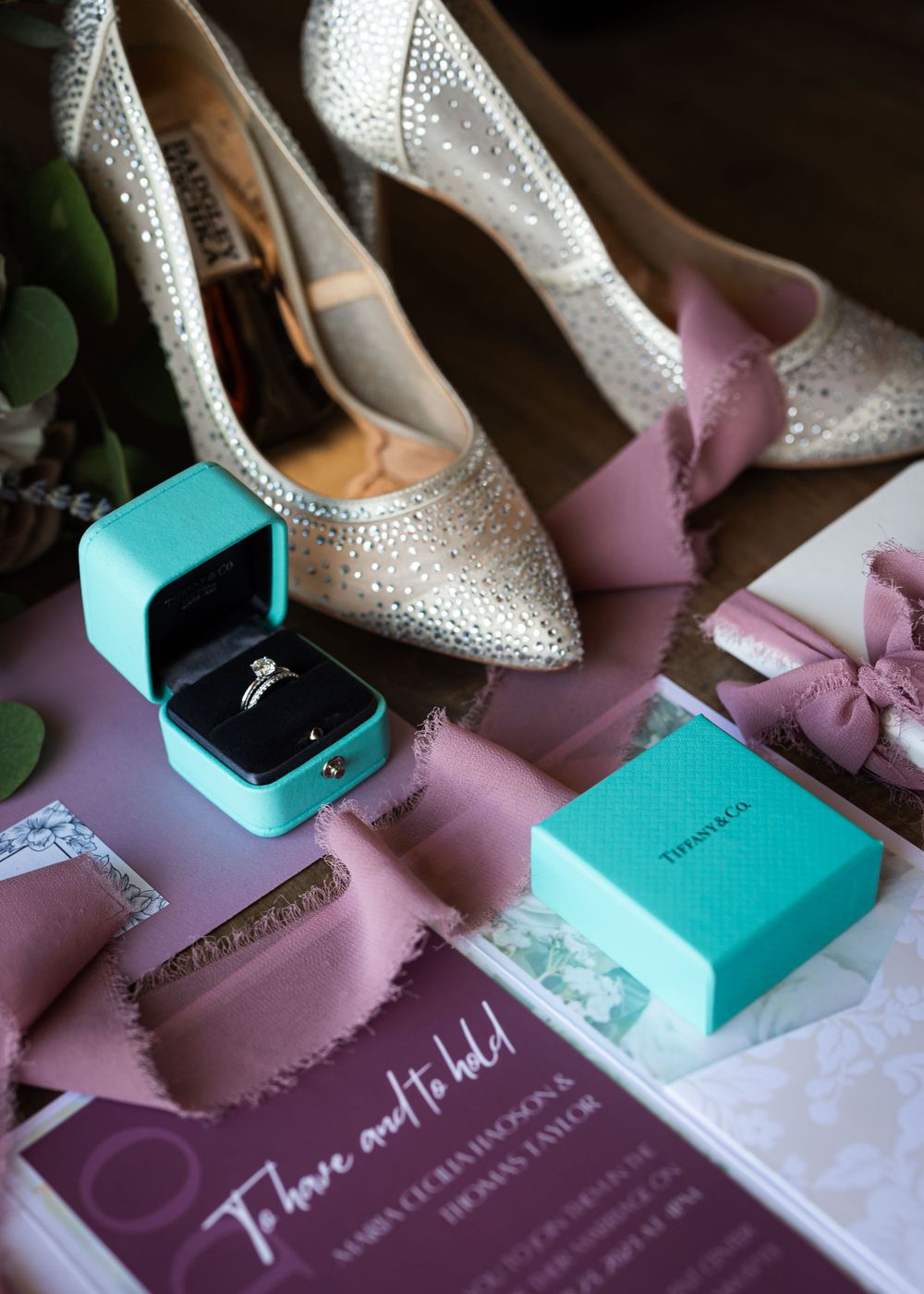 Wedding details with sparkly silver heels, turquoise ring box, and pink invitation on pink background.