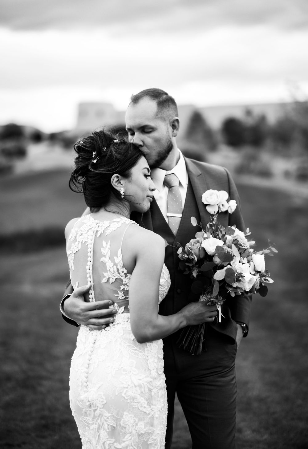 A romantic black and white wedding portrait showing a tender embrace with bouquet.
