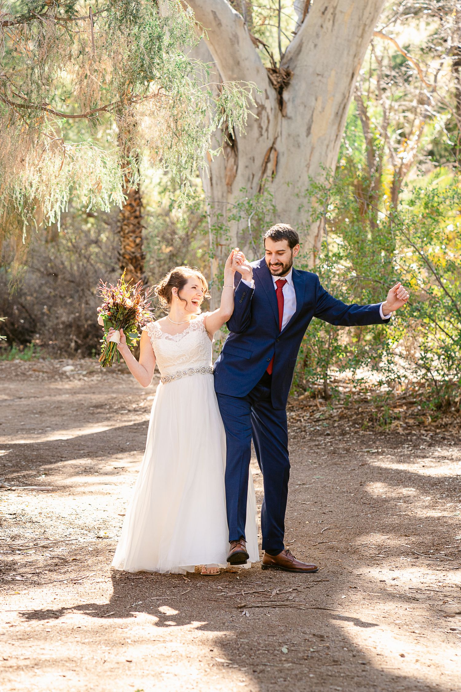 A joyful wedding couple celebrates in a eucalyptus grove with natural lighting.