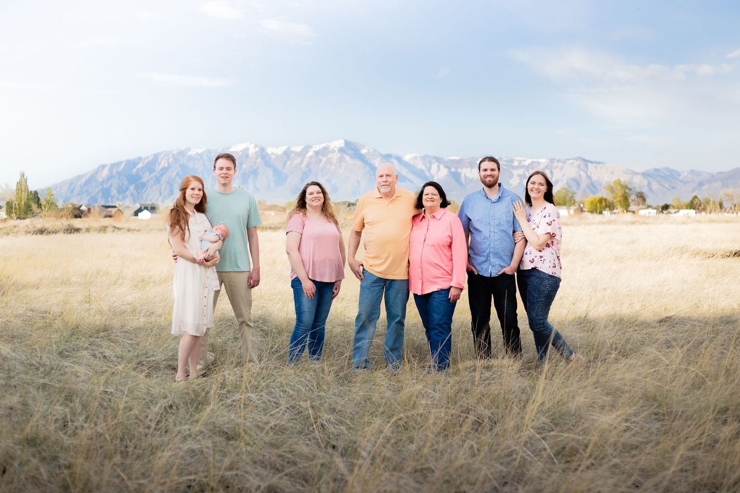 large family with grandparents standing in in field with colorful shirts and a mountain backdrop with blue sky