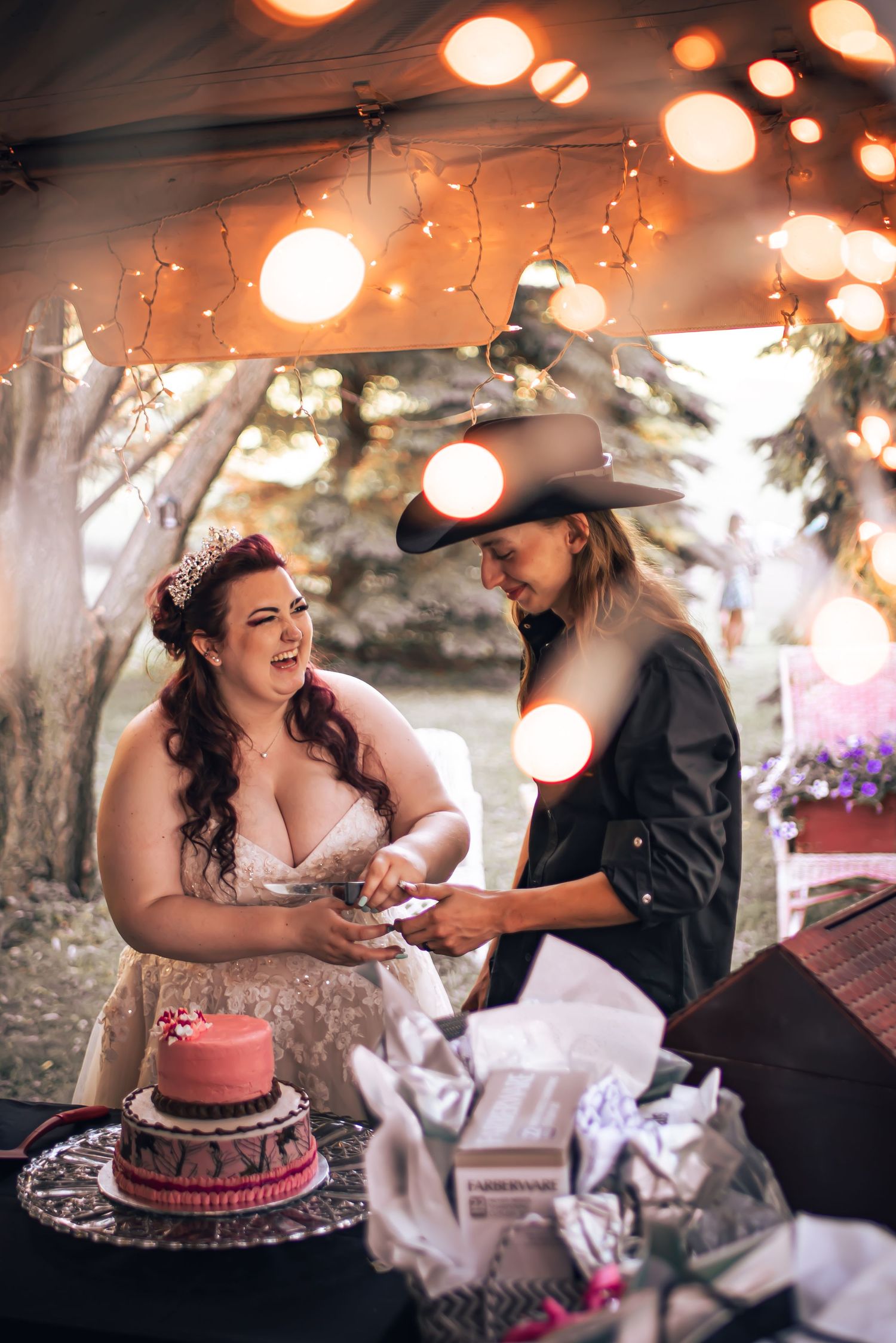 Romantic cake cutting scene with string lights creating warm ambiance at outdoor celebration.