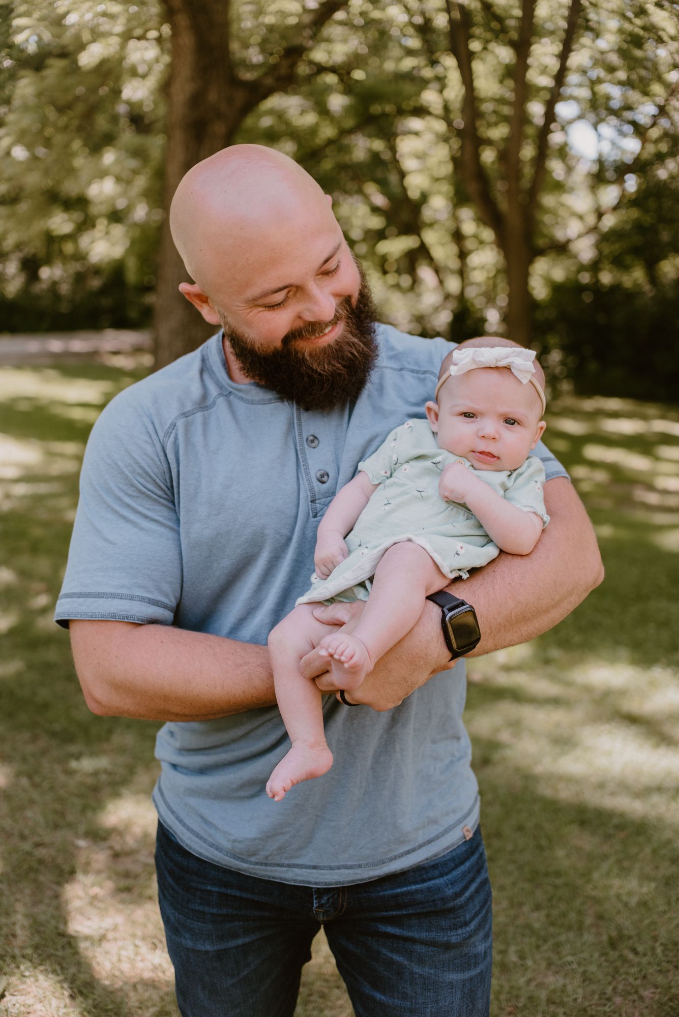 Father in grey polo shirt holding and playing with baby outdoors.