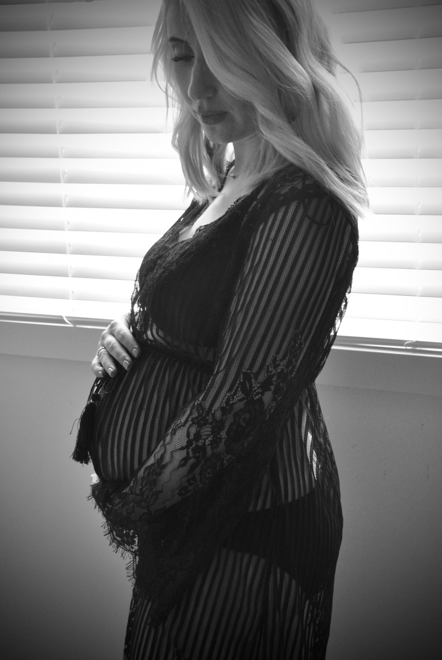 Silhouette of pregnant woman in lace dress standing by window.