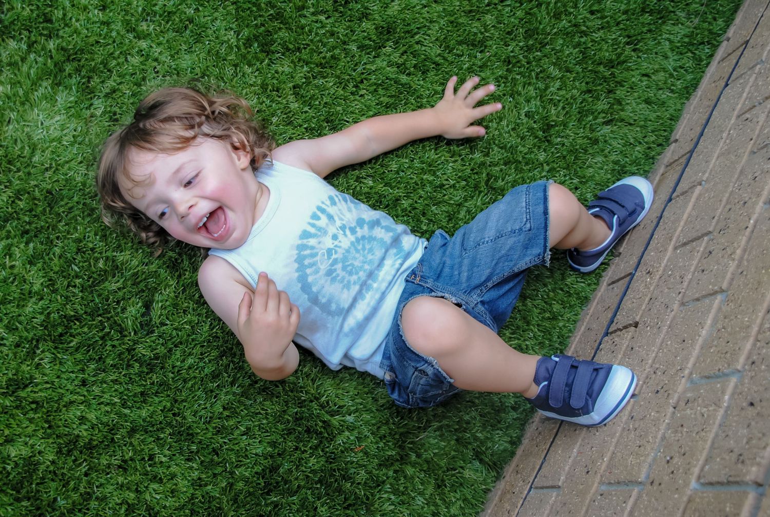 Child lying on artificial grass laughing with arms spread wide.