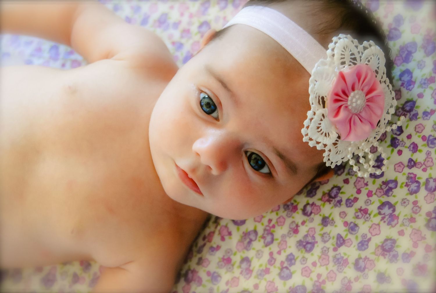 Baby wearing floral lace headband on purple floral blanket.