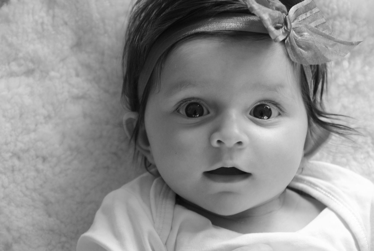 Black and white portrait of baby wearing bow headband.