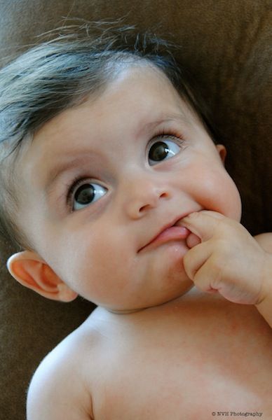 Close up artistic portrait of an infant reaching toward their face against dark background.