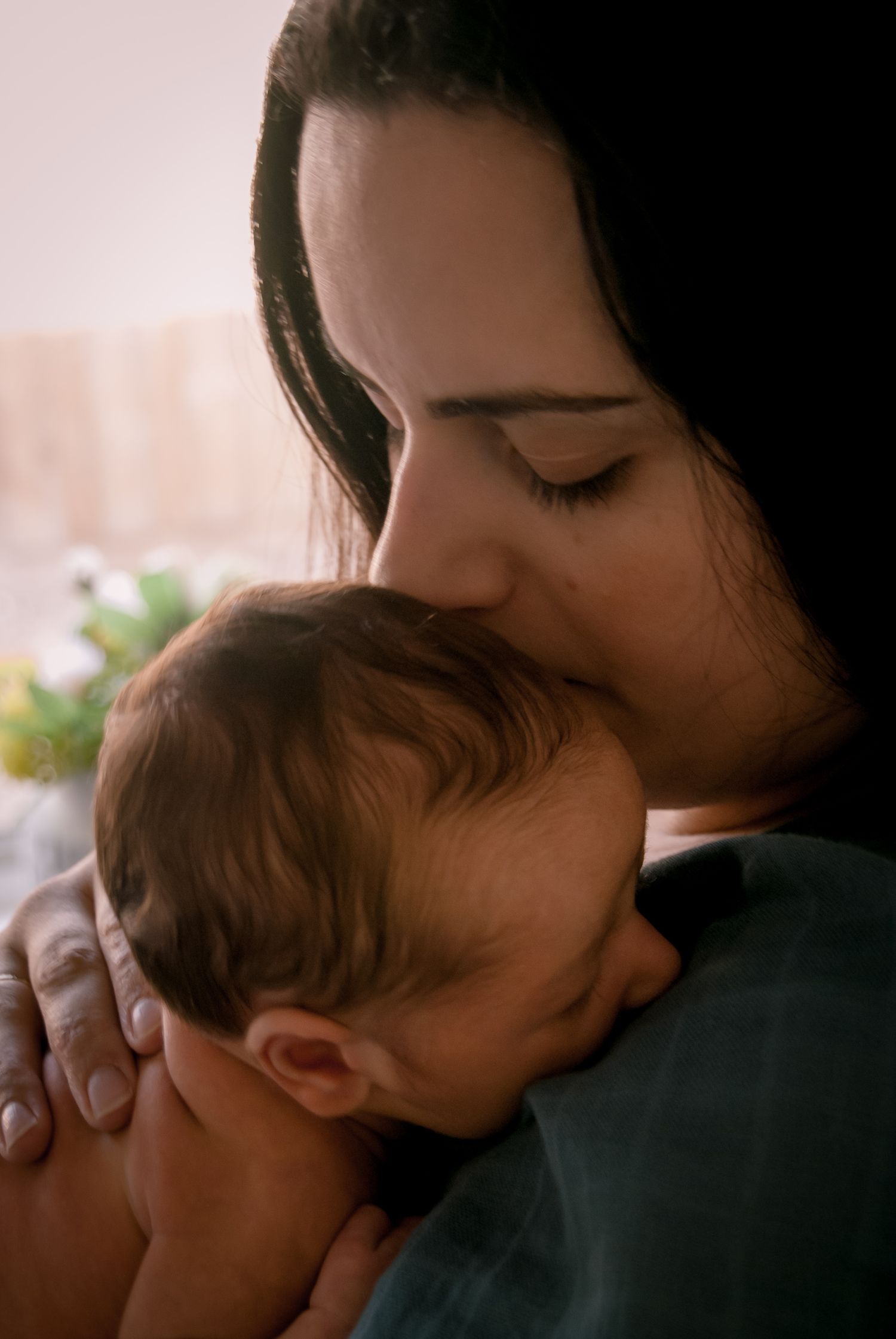 A tender moment captured as a baby nestles against a shoulder in soft natural lighting.