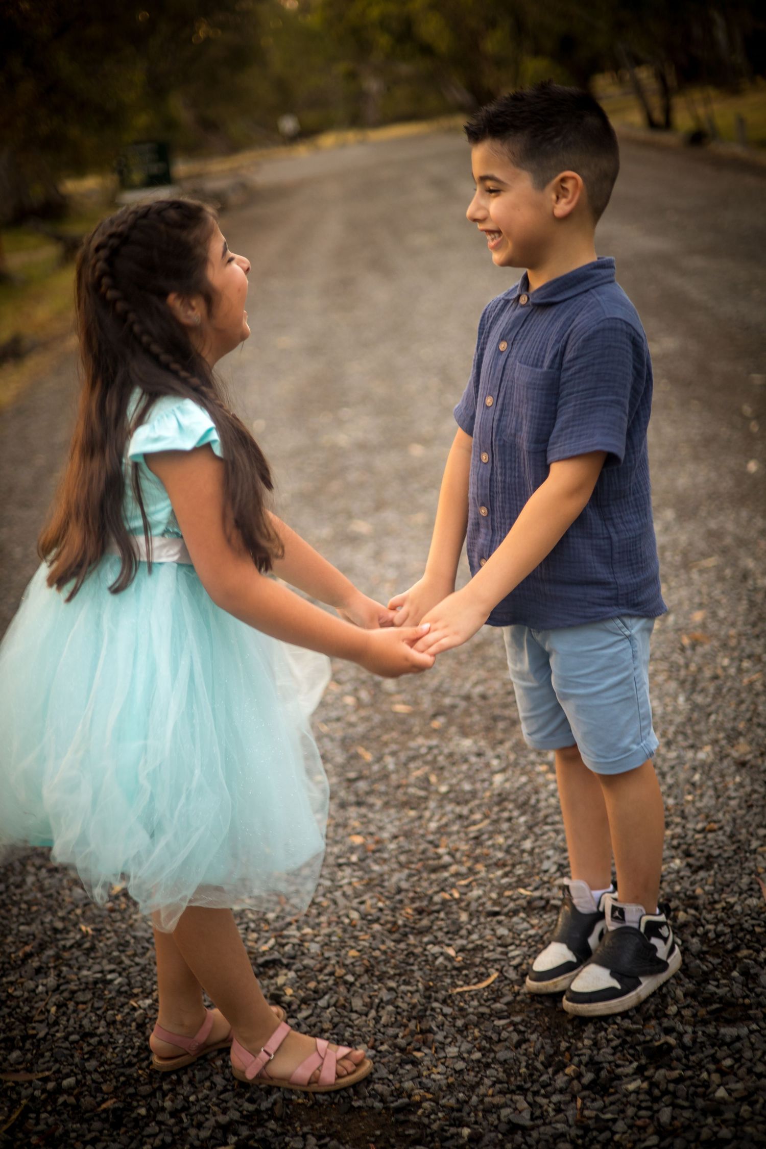 Children playing and holding hands on gravel path while wearing casual clothes and tulle skirt.
