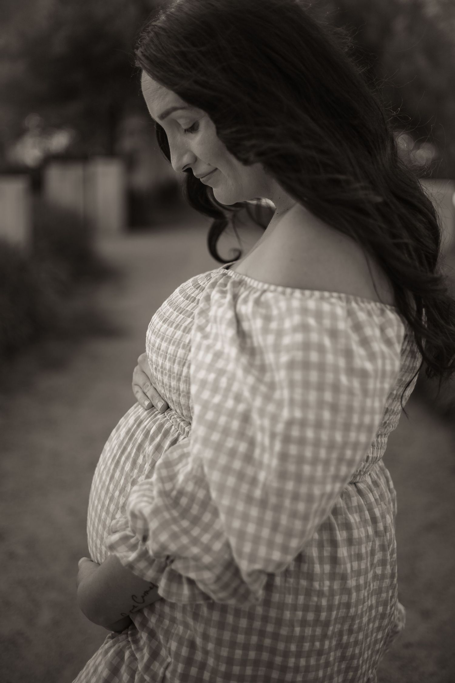 Side profile of a pregnant woman wearing a gingham dress in black and white photography.