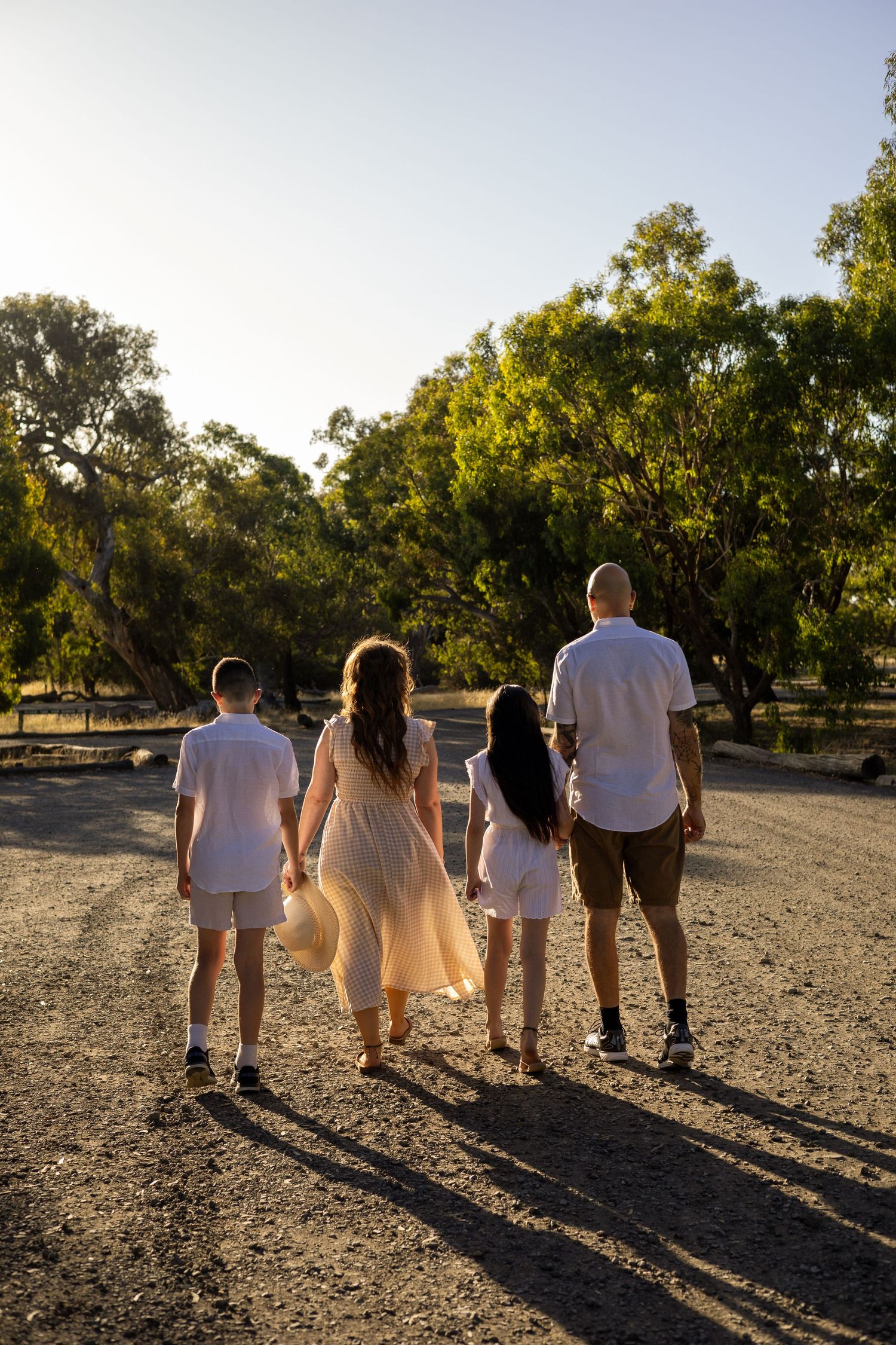 Family walking together on dirt path at sunset with trees in background.