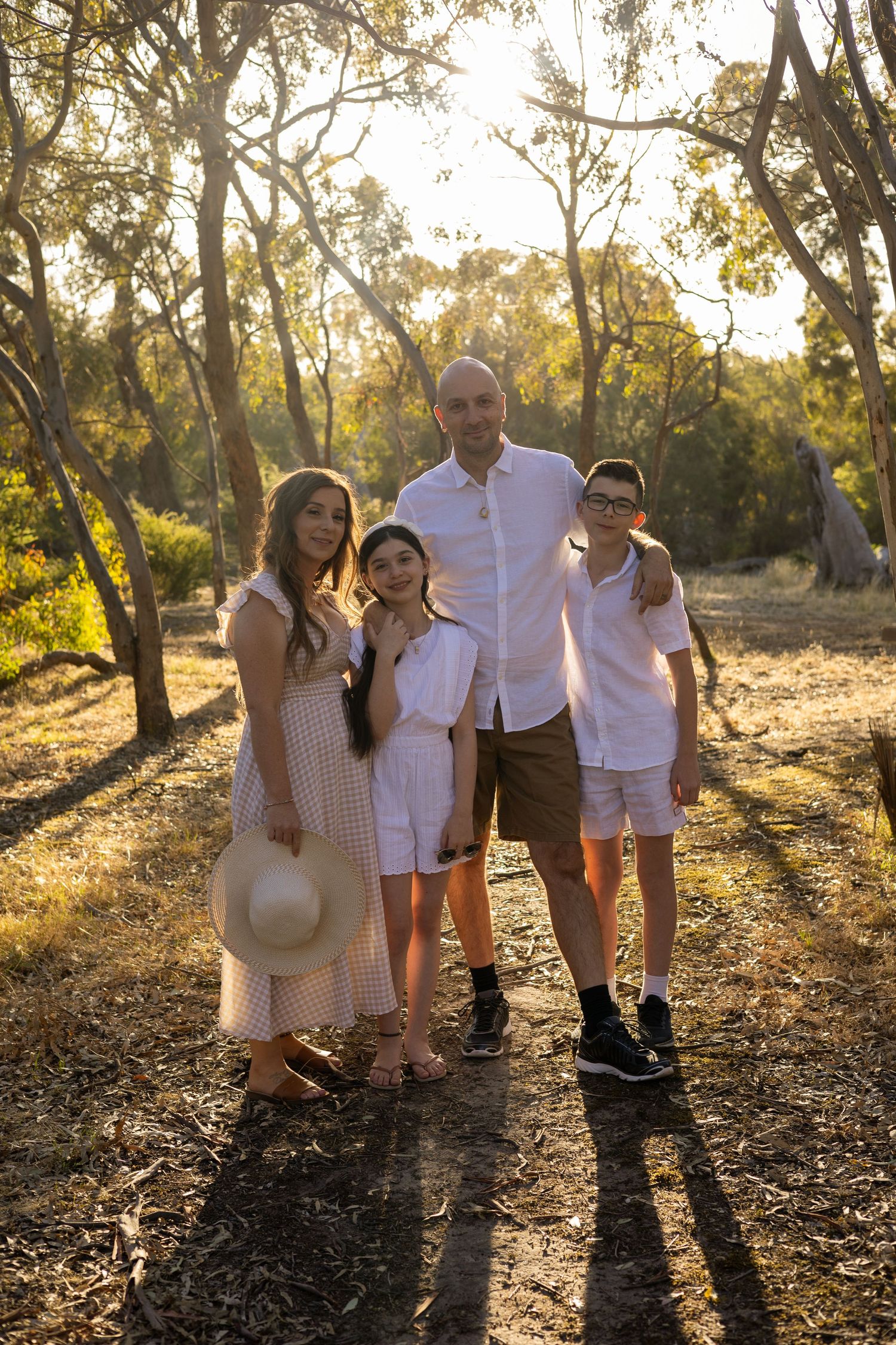 Family poses for outdoor portrait in wooded area during sunset light.