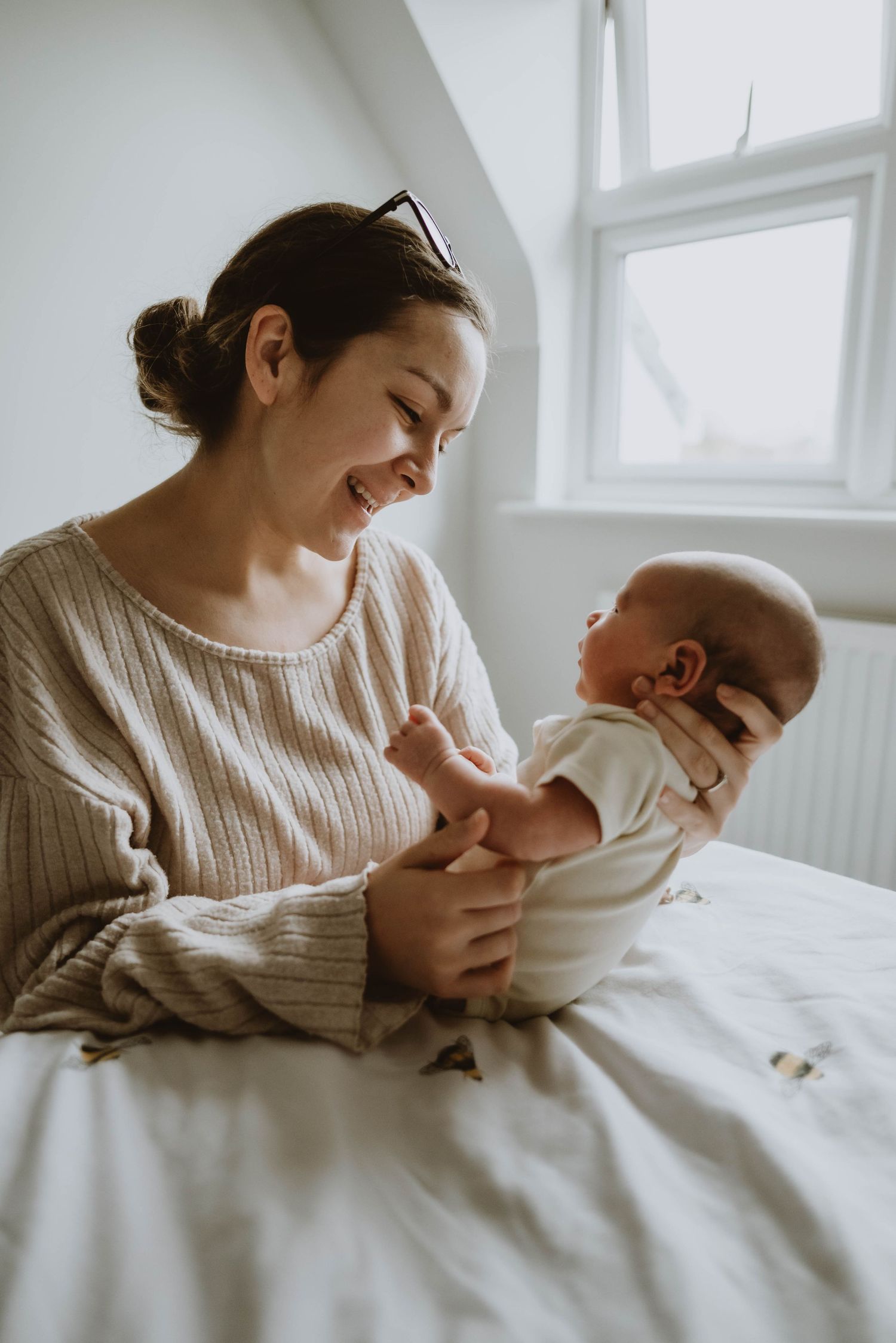 A tender moment between parent and baby in a bright sunlit room with white bedding.