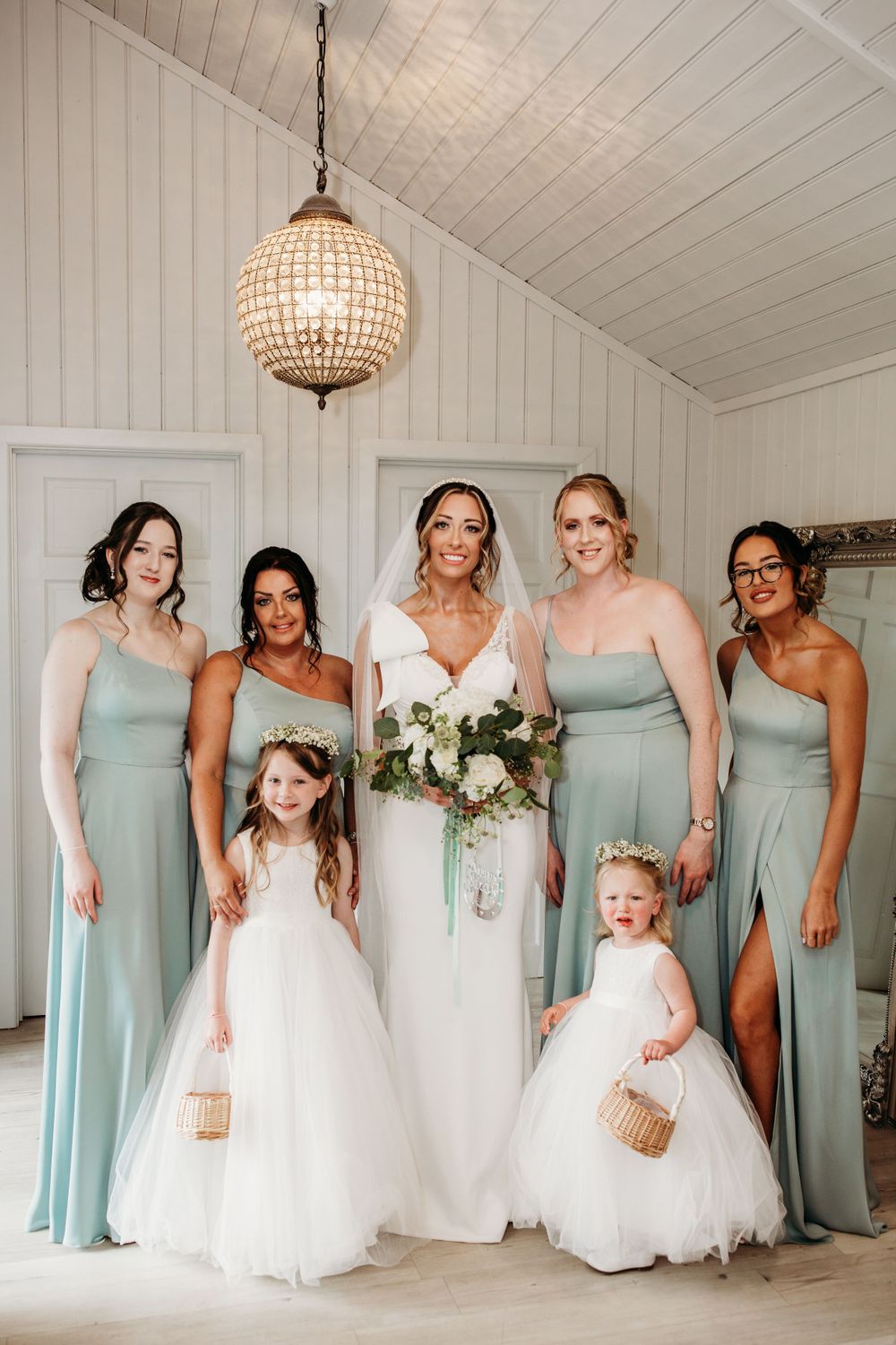 Bridal party in mint green dresses poses with flower girls in white tulle dresses.