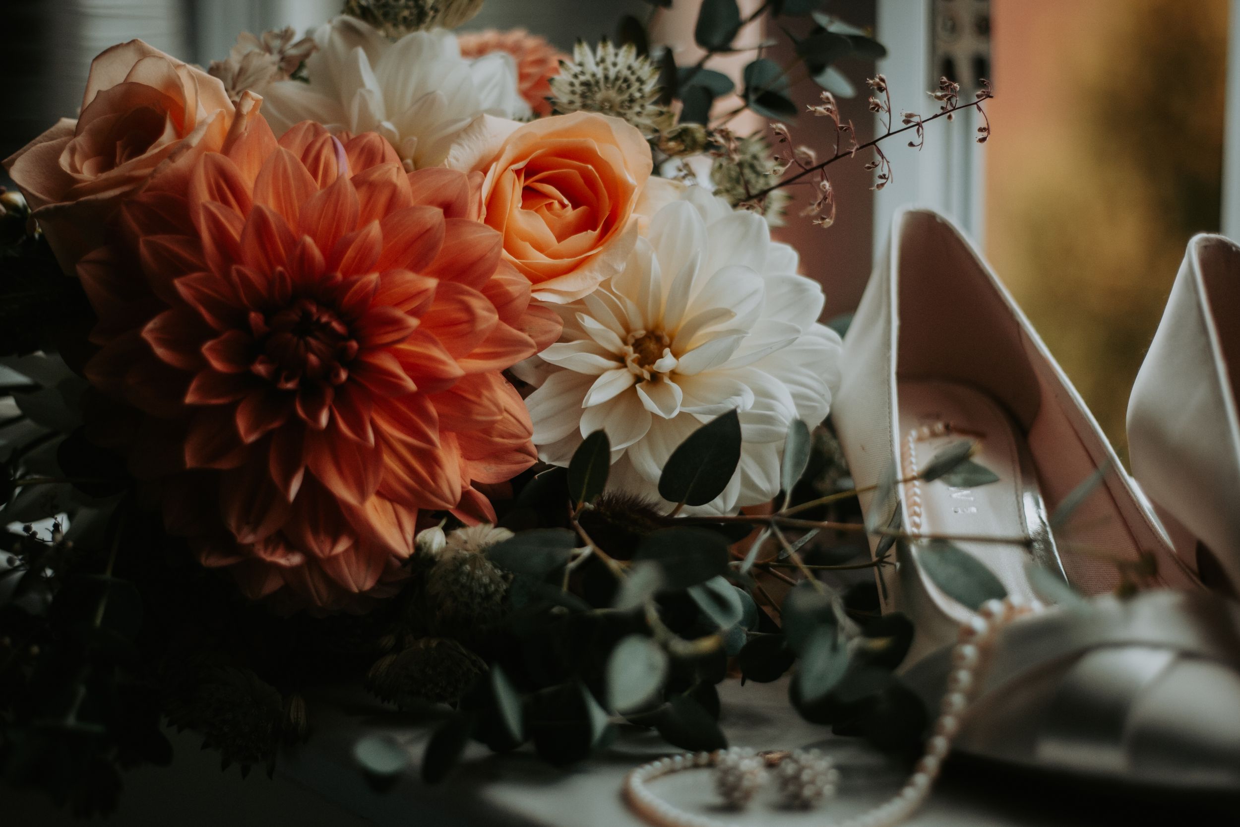 Peach and coral colored floral arrangements with dahlias and roses in soft lighting.